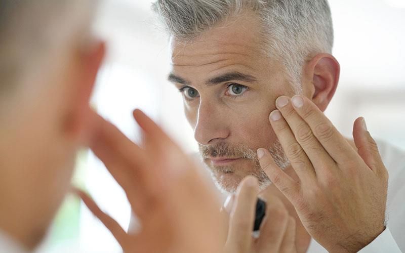 Ein Mann betrachtet sein Gesicht im Spiegel.