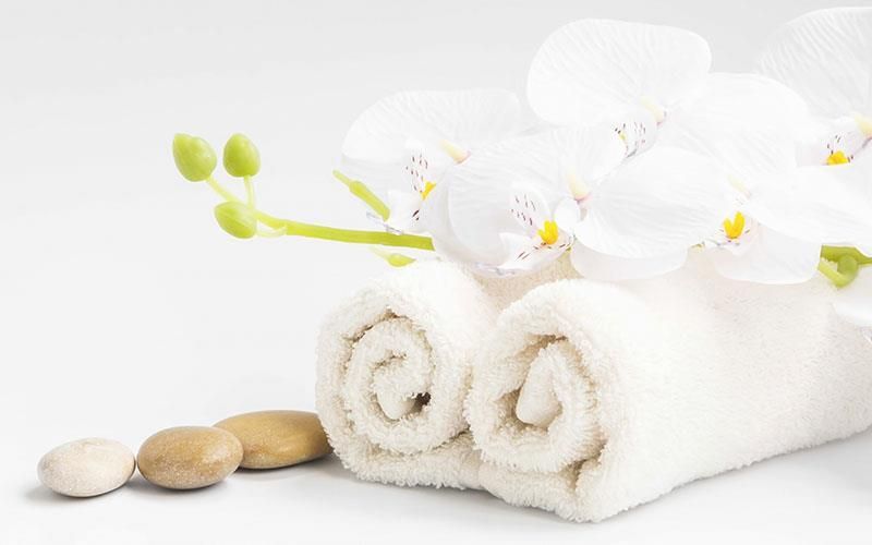 Zwei gerollte Handtücher mit weißen Orchideen und Steinen auf weißem Hintergrund.