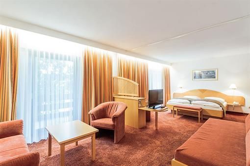 Ein Hotelzimmer mit Couch, Sessel, Tisch und Fernseher.