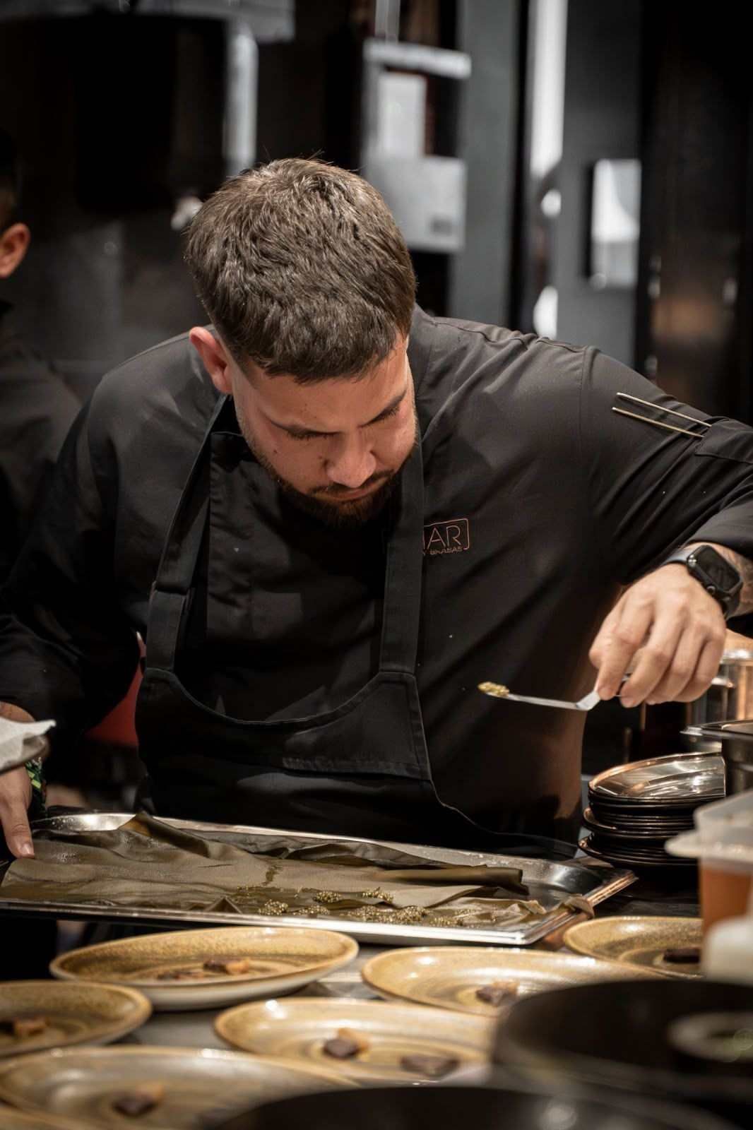 Un chef emplata los alimentos en la cocina de un restaurante, concentrado sobre un mostrador con varios platos.