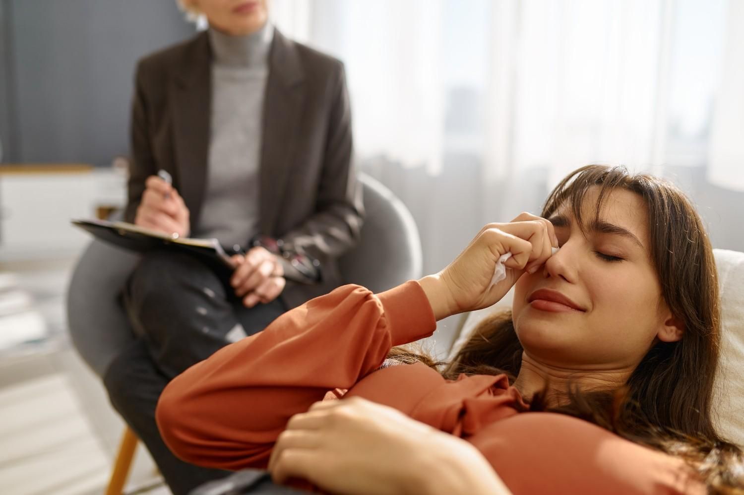 Mujer acostada, llorando en terapia; el terapeuta toma notas.