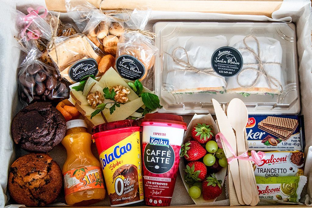 Cesta de regalo con artículos de alimentación: bollería, zumo, bebida de café, bocadillos, fruta, galletas.