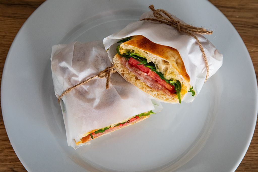 Mitades de sándwich envueltas en papel blanco sobre un plato blanco, atadas con cordel.
