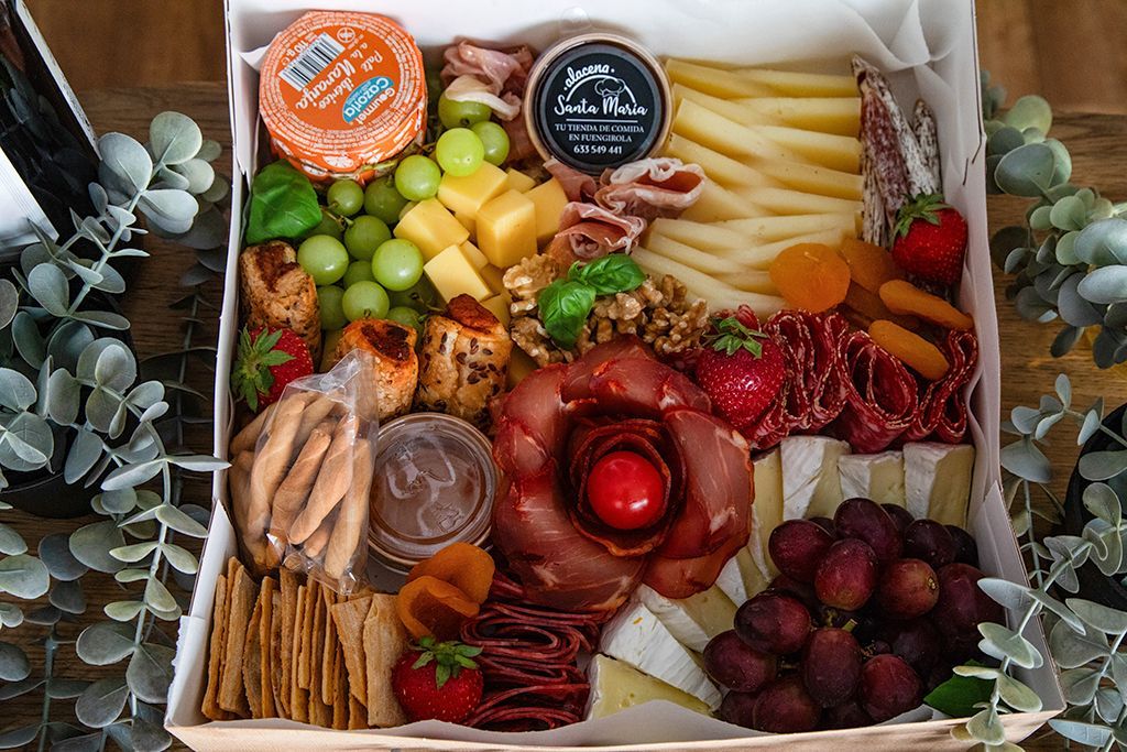 Tabla de embutidos con uvas, quesos, galletas y carnes, en caja.