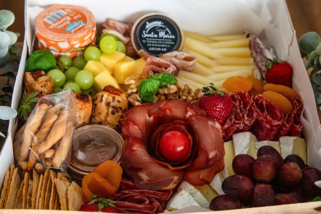 Caja de charcutería con surtido de quesos, carnes, frutas, frutos secos, galletas y salsa.