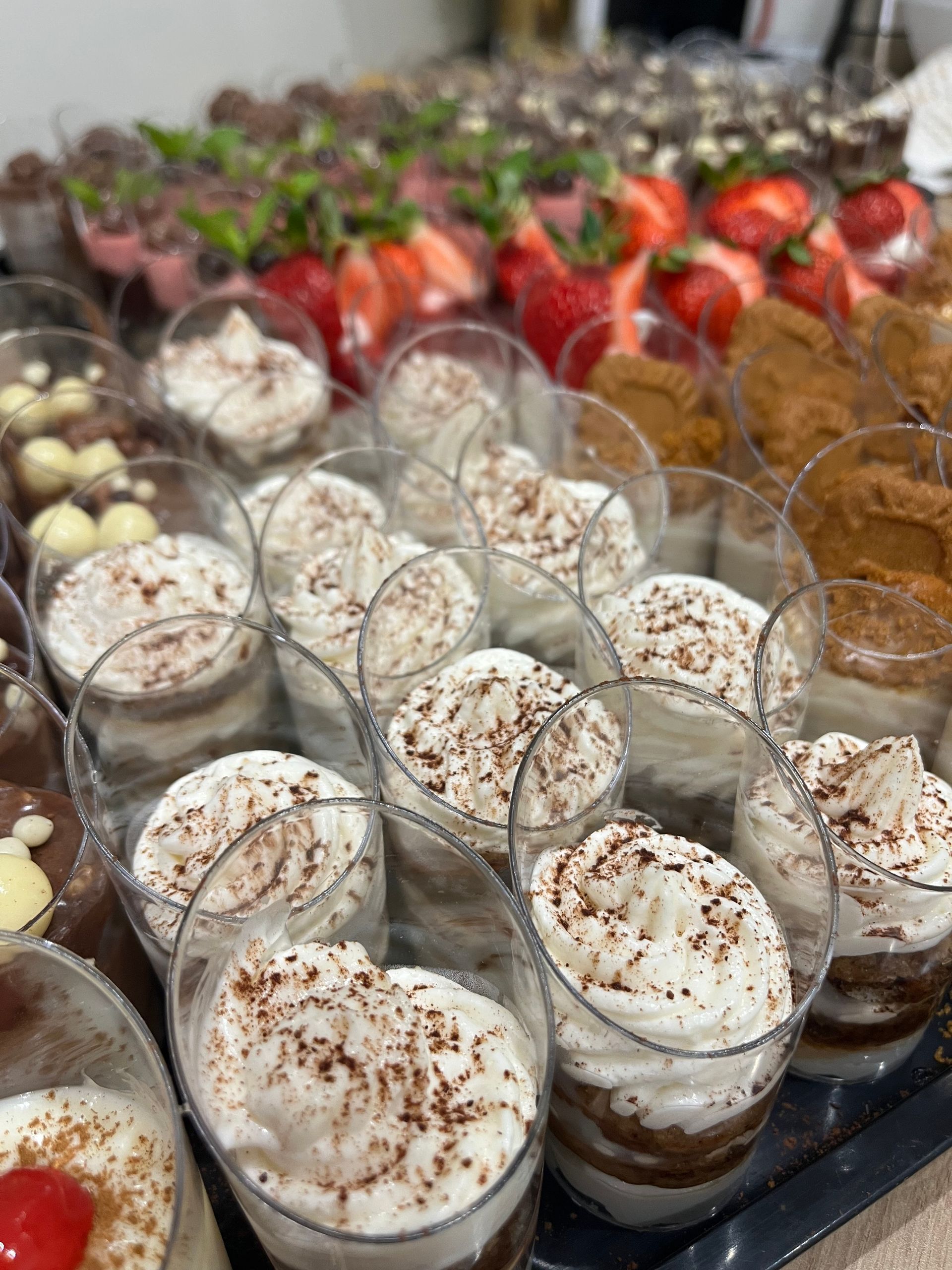 Bandeja de postres individuales variados: mousse, fresas, nata montada y tiramisú en vasitos transparentes.