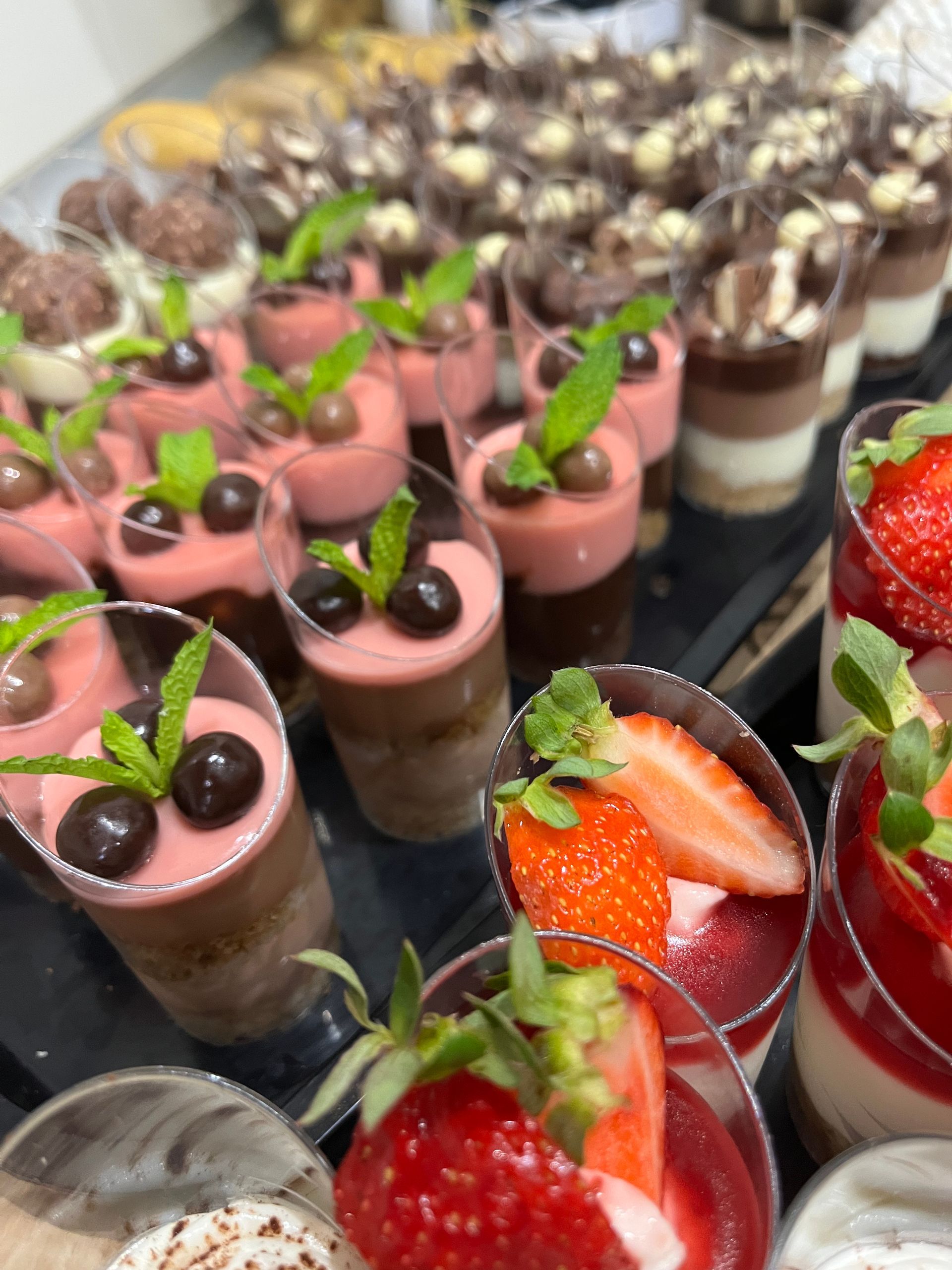 Bandeja de mini postres en vasos transparentes con decoración de chocolate, fresa y menta.