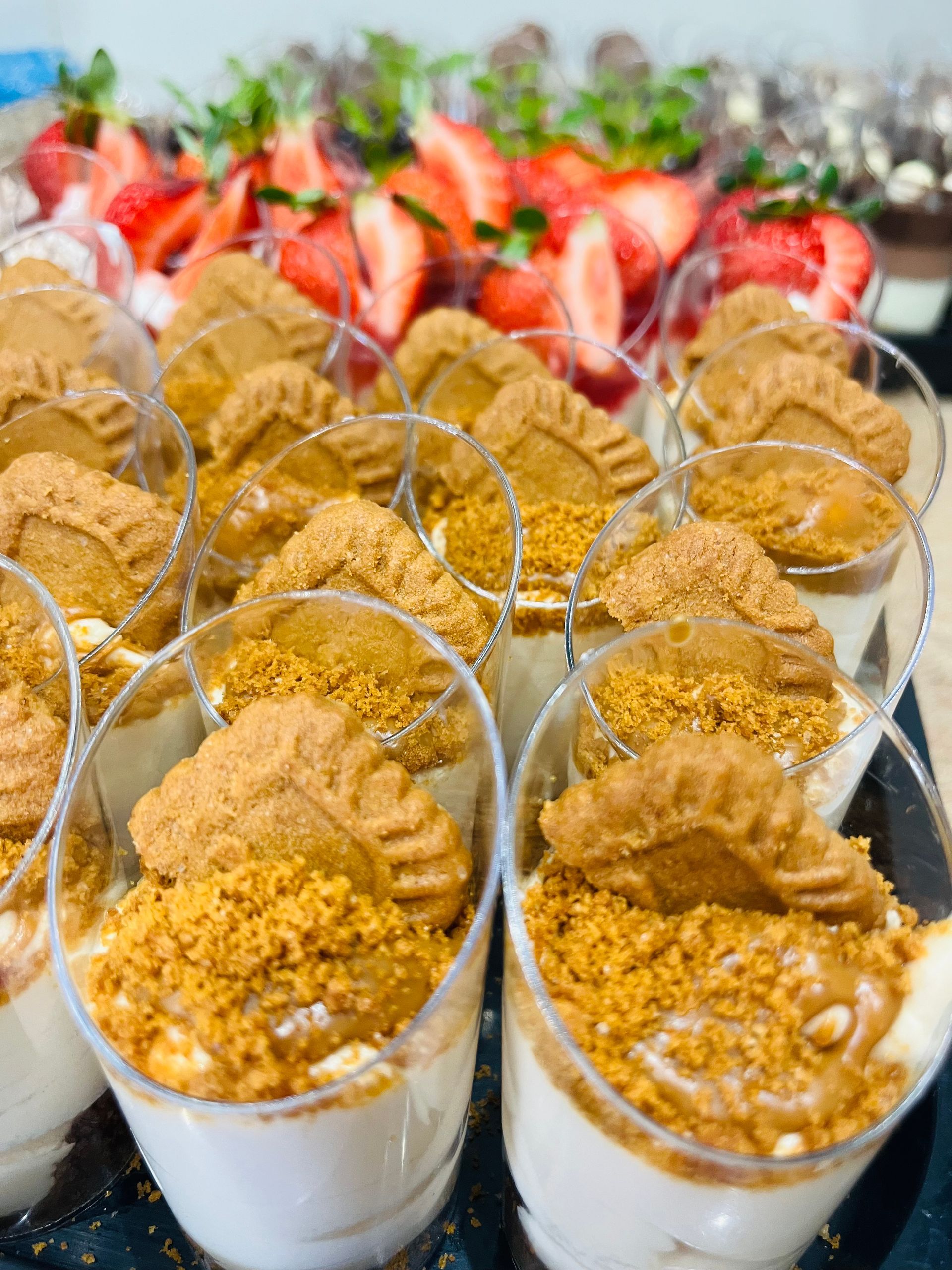 Copas de postre con crema, galletas trituradas y una galleta entera; fresas en el fondo.