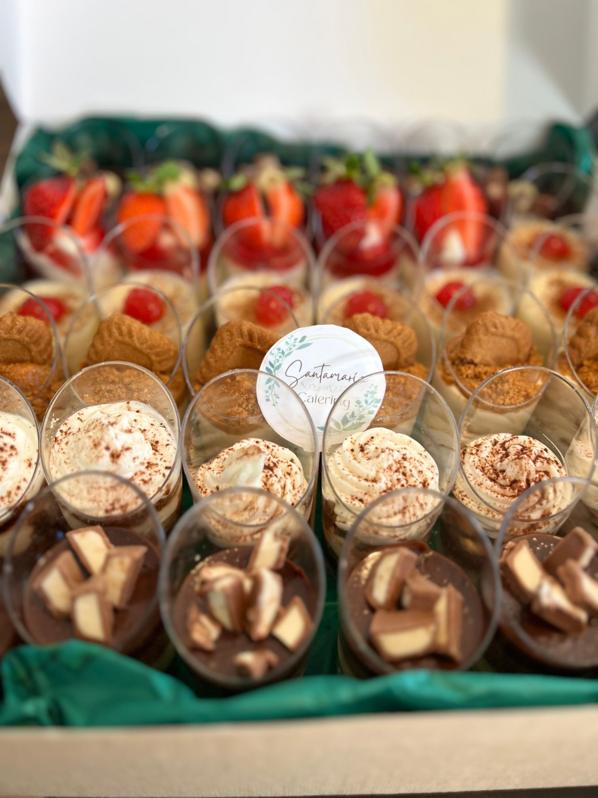 Caja de postres con capas de diversos dulces que incluyen fresas, pasteles y tazas de chocolate.