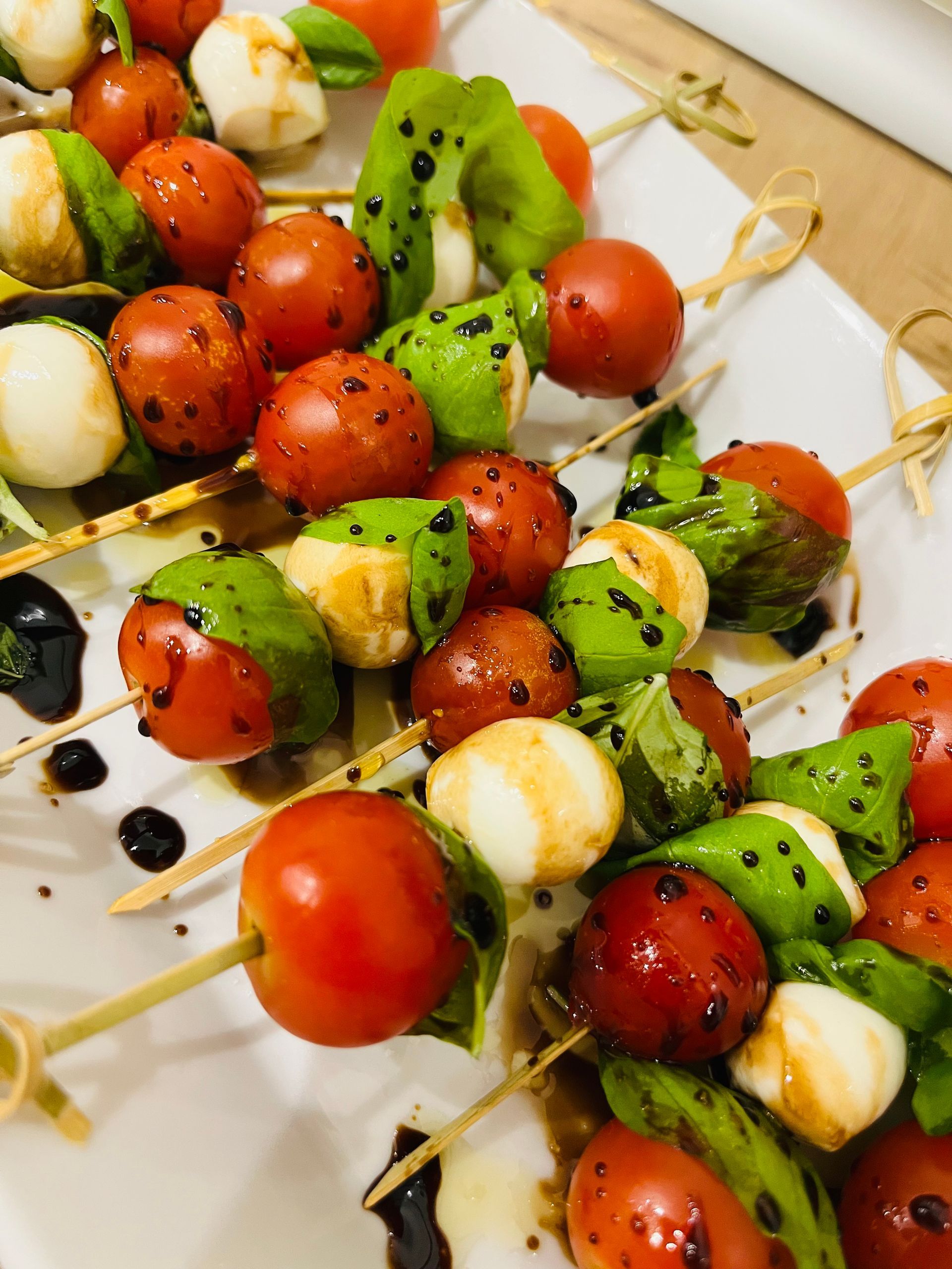 Brochetas Caprese: tomates cherry, bolitas de mozzarella, albahaca, rociadas con glaseado balsámico.