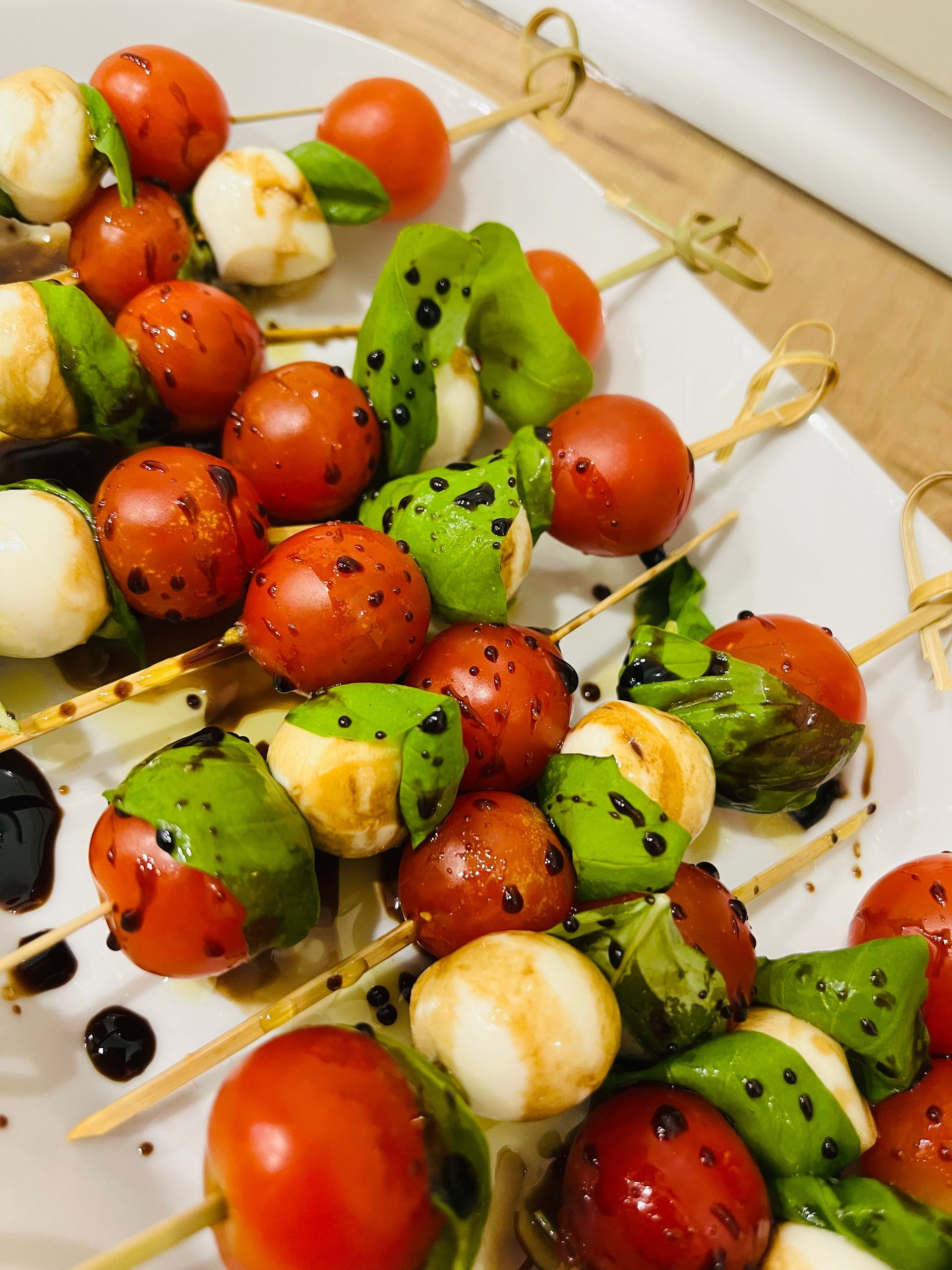 Brochetas Caprese: tomates cherry, bolitas de mozzarella, albahaca y kiwi en brochetas de madera, rociadas con glaseado balsámico.