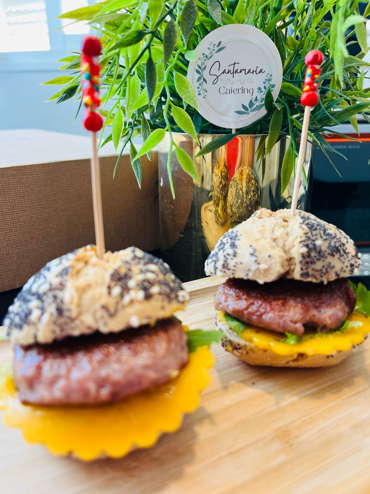 Hamburguesas en miniatura con panecillos, hamburguesas, queso, lechuga y brochetas, sobre una tabla de madera.