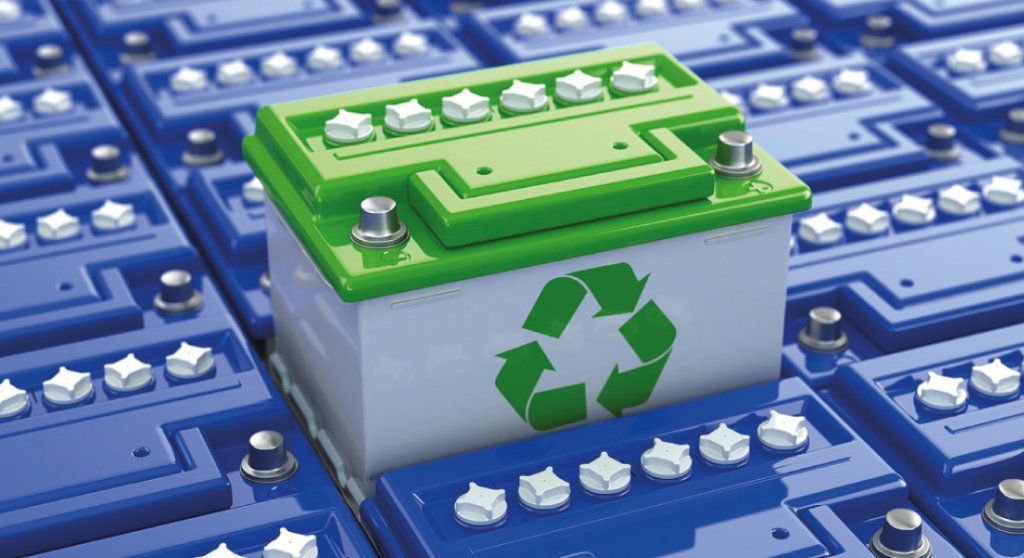 Una batería verde y blanca con un símbolo de reciclaje está encima de una pila de baterías azules.