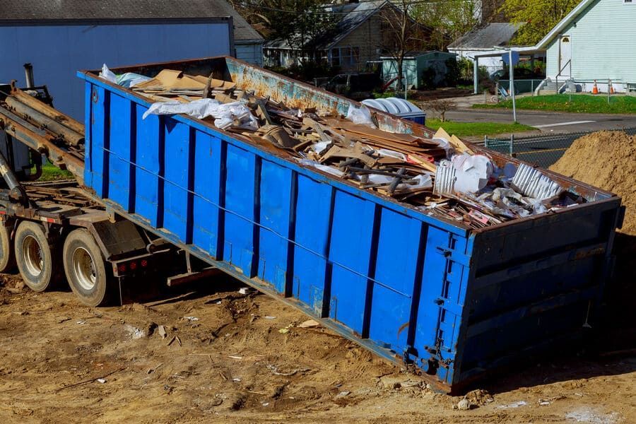 Un contenedor de basura azul está encima de un campo de tierra.