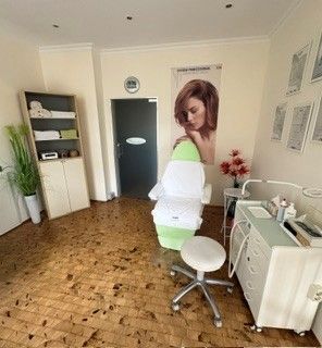 Innenansicht eines Schönheitssalons mit einer Person, die neben einem weißen Stuhl und einem Frisierplatz steht.
