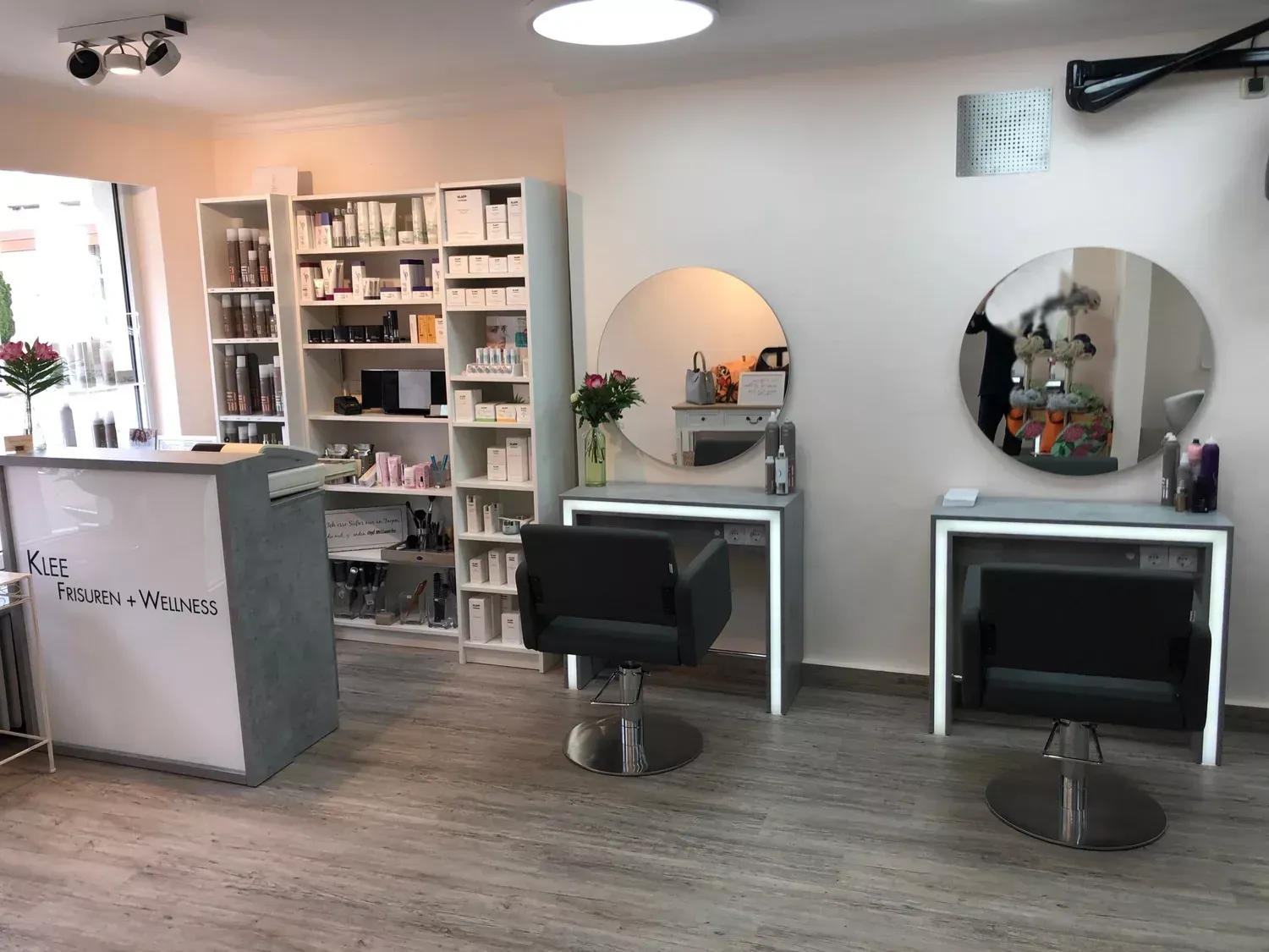 Heller Saloninnenraum mit Friseurstühlen, Spiegeln, Regalen und einem Empfangstresen auf Holzboden.