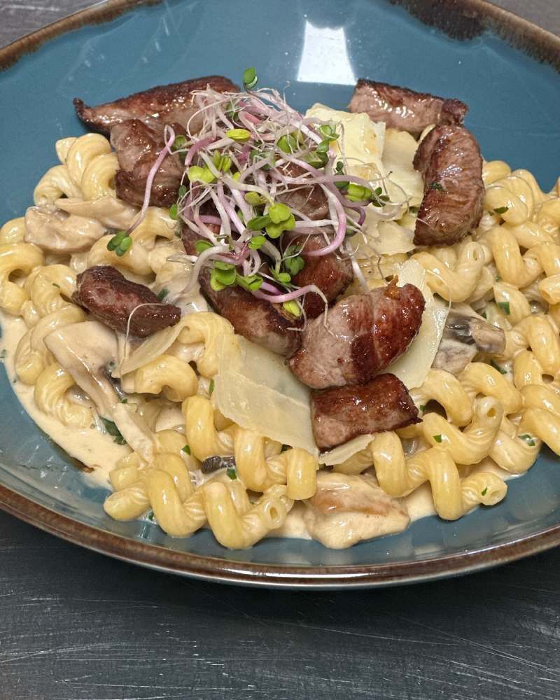 Ein Teller mit Makkaroni und Käse, Fleisch und Pilzen auf einem Tisch. Foto von Zum Freihof Ristorante Pizzeria