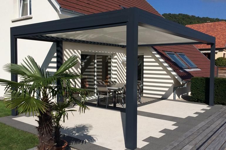 Patio moderne avec pergola grise, table et chaises et palmier en pot à côté d'une maison.