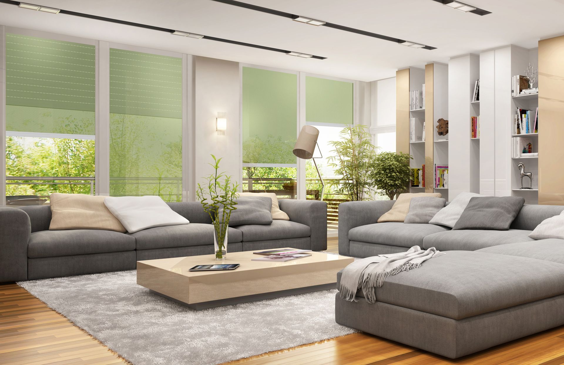 Salon moderne et lumineux avec canapés gris, table basse beige et grandes fenêtres laissant entrer la lumière du soleil.