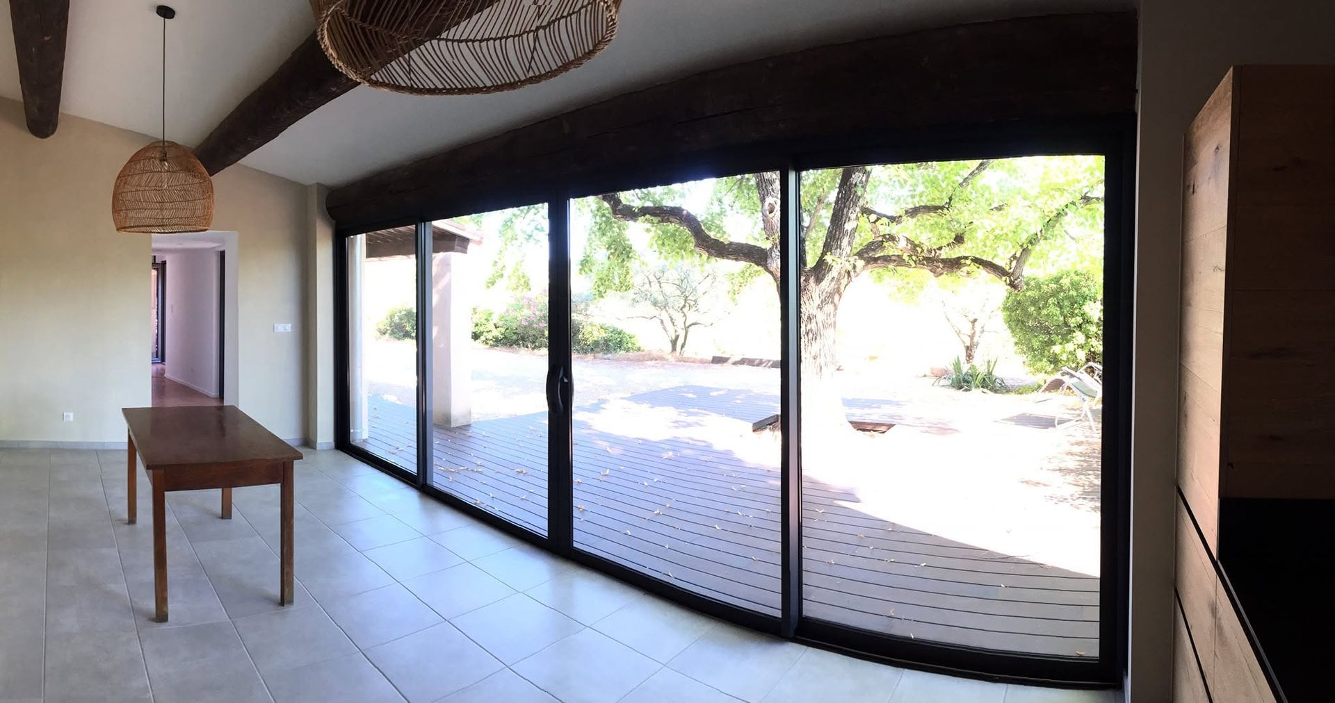 Pièce de vie moderne et lumineuse avec de grandes portes vitrées donnant sur un patio ensoleillé et des arbres à l'extérieur.