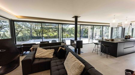 Salon moderne avec canapé noir, poêle à bois et baies vitrées panoramiques.