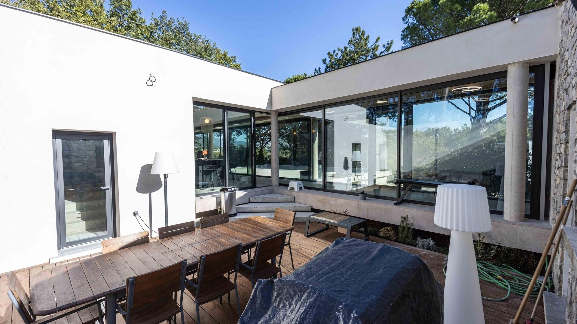 Terrasse moderne avec table à manger extérieure, chaise longue et grandes baies vitrées par une journée ensoleillée.