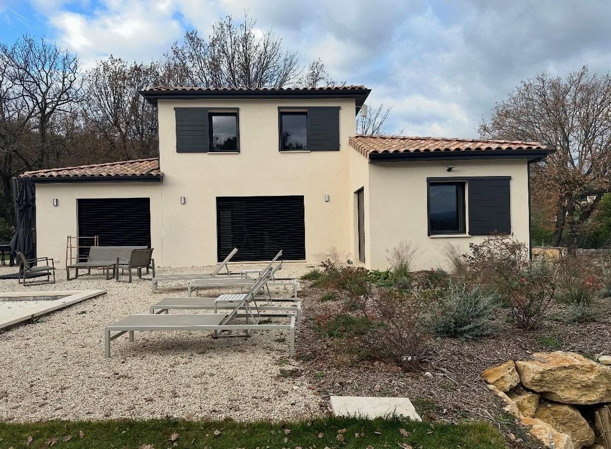 Maison à étage avec de grandes fenêtres dans un jardin gravillonné.