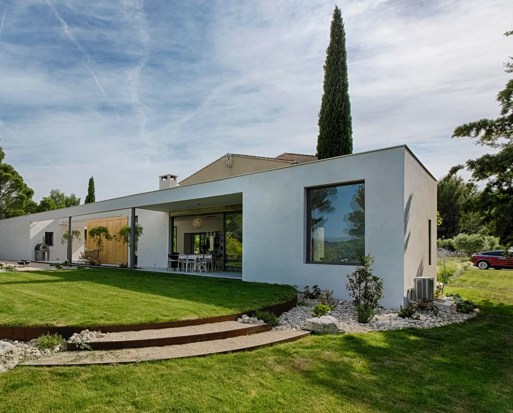 Maison blanche moderne avec toit plat, grandes fenêtres et pelouse verte avec marches en pierre à l'avant.
