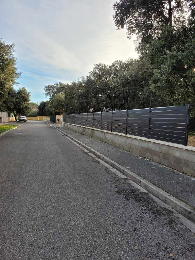 Rue bordée d'un mur en béton et d'une clôture en aluminium.
