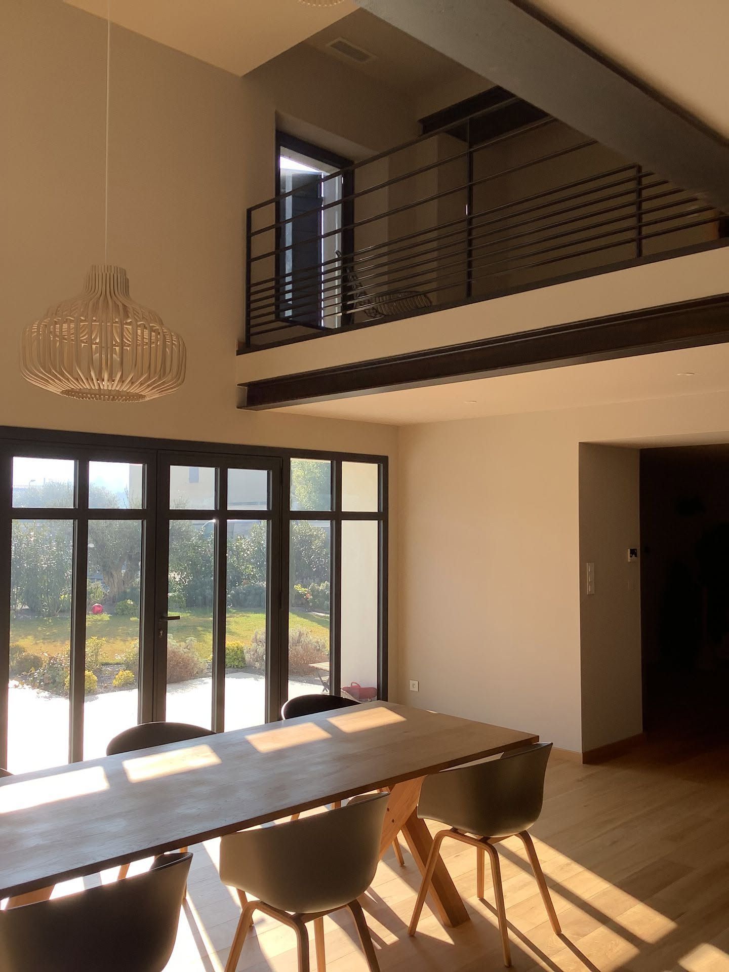 Salle à manger moderne avec de grandes fenêtres, une longue table en bois, des chaises noires et un balcon en mezzanine.