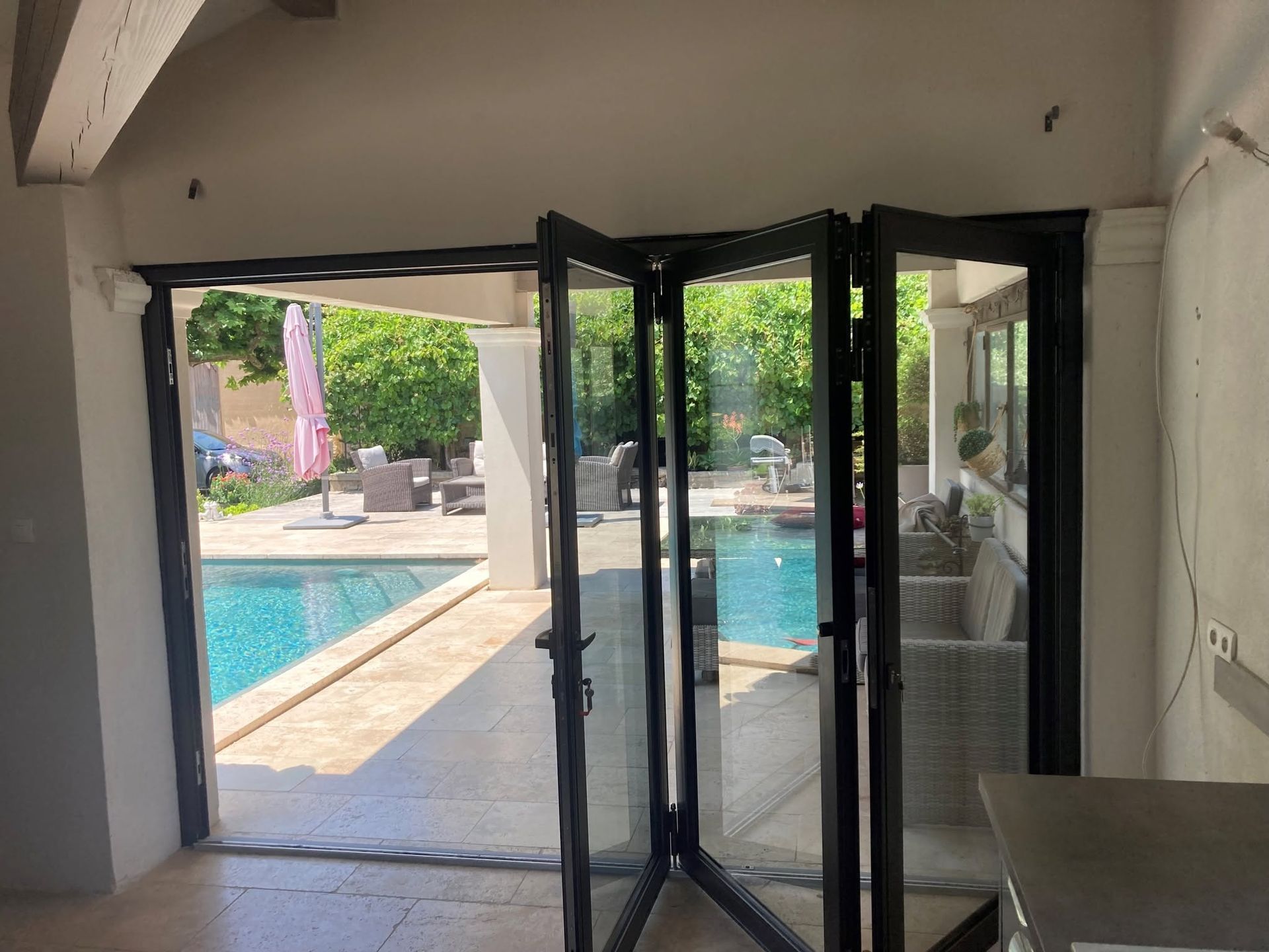 Portes oscillo-battantes donnant sur une terrasse ensoleillée avec piscine et mobilier de jardin.