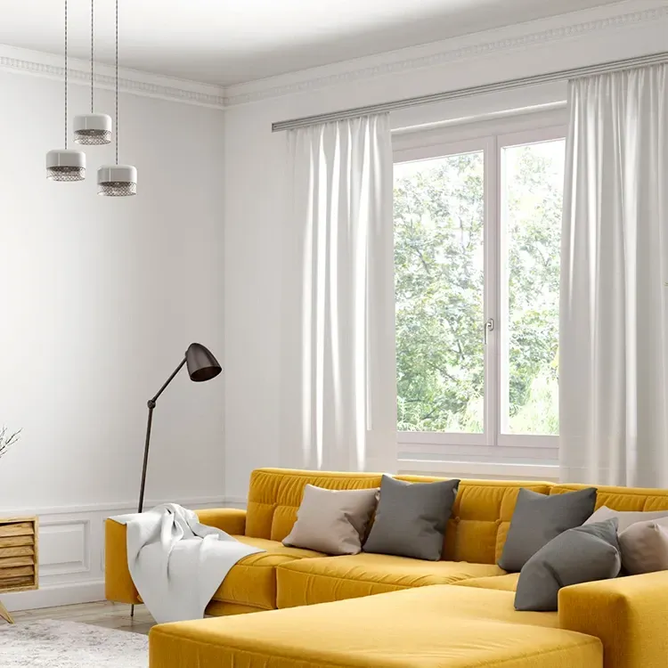 Salon lumineux avec un canapé d'angle jaune moutarde, des murs blancs et une grande fenêtre avec des rideaux.