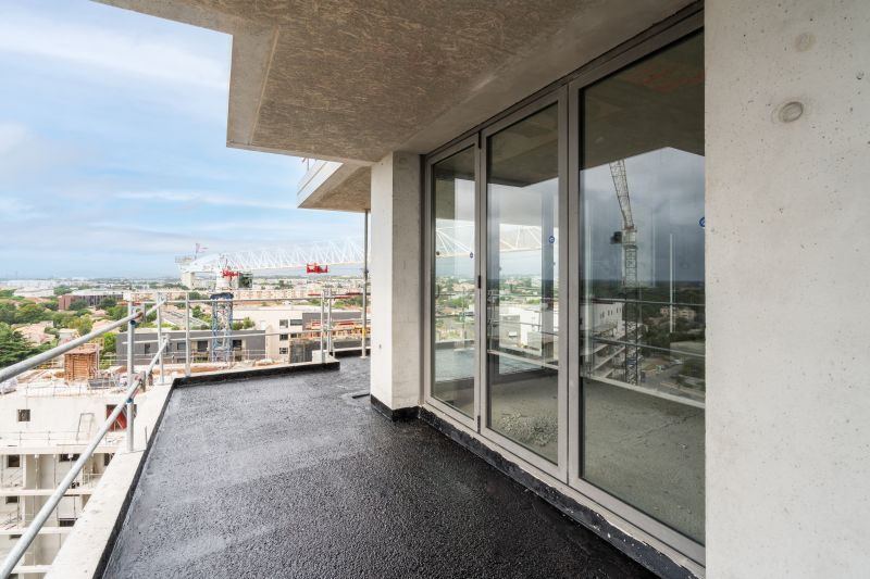 Balcon d'appartement avec sol foncé, baie vitrée et vue sur la ville au-delà de la rambarde.