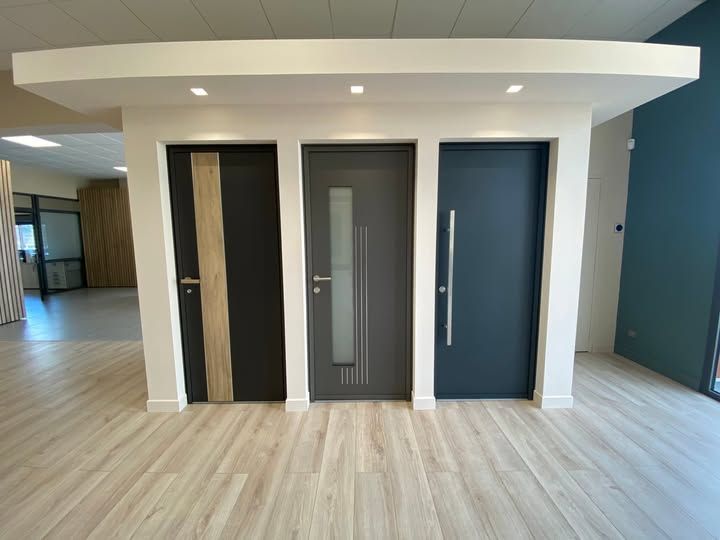 Kiosque de showroom avec trois portes : noire, grise avec vitre et bleue, sur un parquet clair.