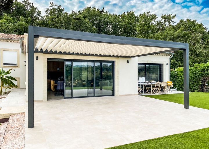 Patio blanc moderne avec pergola foncée et baies coulissantes en verre donnant sur une terrasse de jardin.