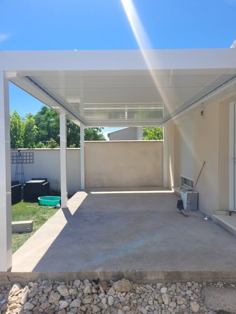 Pergola blanche adossée au mur d'une maison avec sol en béton et ciel d'un bleu éclatant.