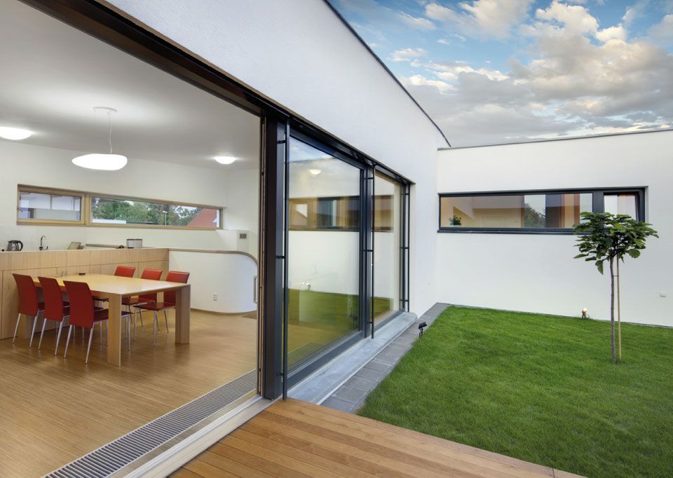 Patio moderne avec baies coulissantes en verre, table en bois, coin repas intérieur et petite cour gazonnée.