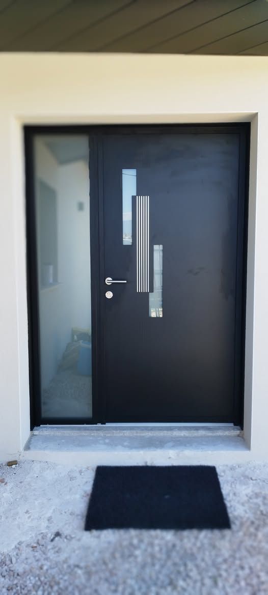 Entrée principale avec une porte moderne sombre, des impostes latérales et un paillasson noir sur un porche en béton.