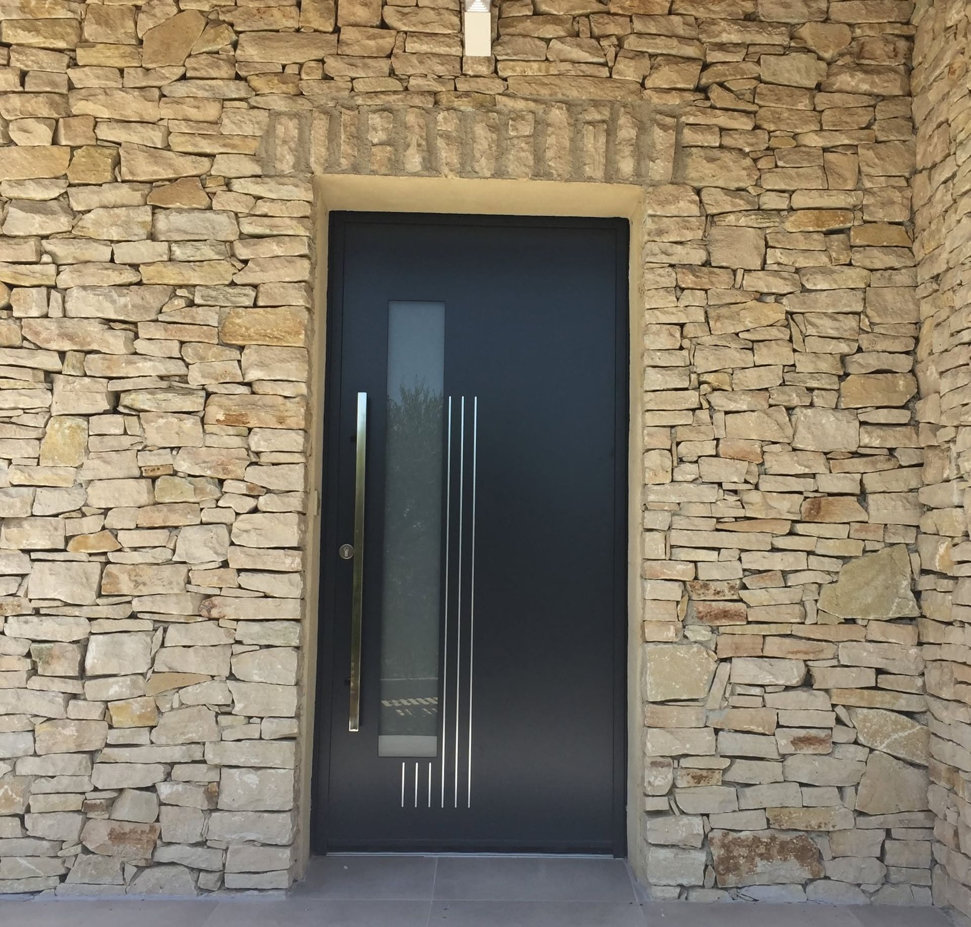 Mur extérieur en pierre avec une porte d'entrée moderne, une poignée bâton de maréchal et panneaux de verre dépoli.