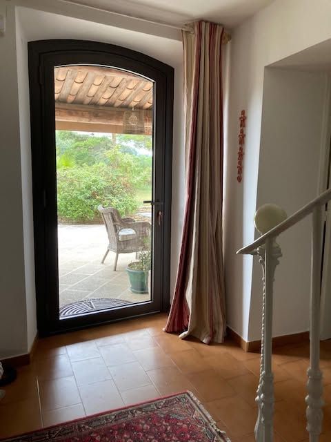 Porte vitrée cintrée donnant sur un patio, une chaise et une végétation luxuriante.