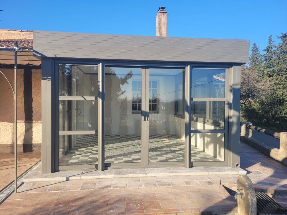 Véranda avec cadre gris et portes coulissantes avec carrelage décoratif et terrasse.