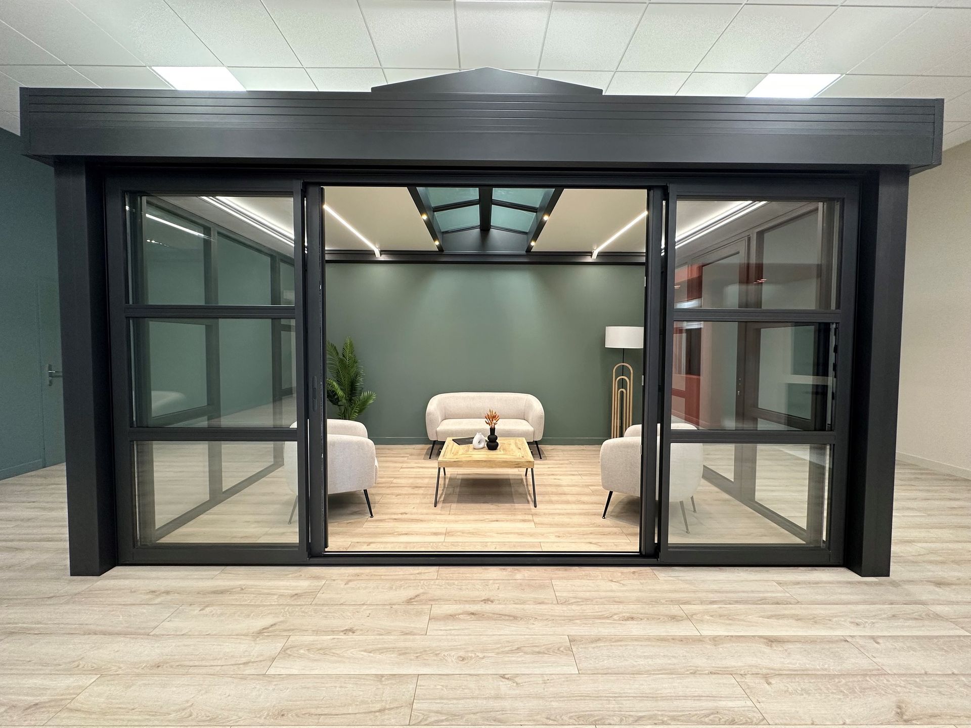 Véranda moderne avec fenêtres ouvertes, fauteuil beige et encadrement sombre dans un espace intérieur carrelé.