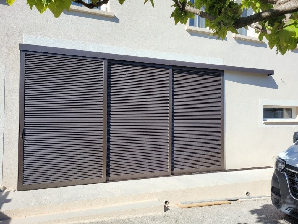 Extérieur d'une maison moderne avec de grands volets coulissants et une voiture garée à droite.