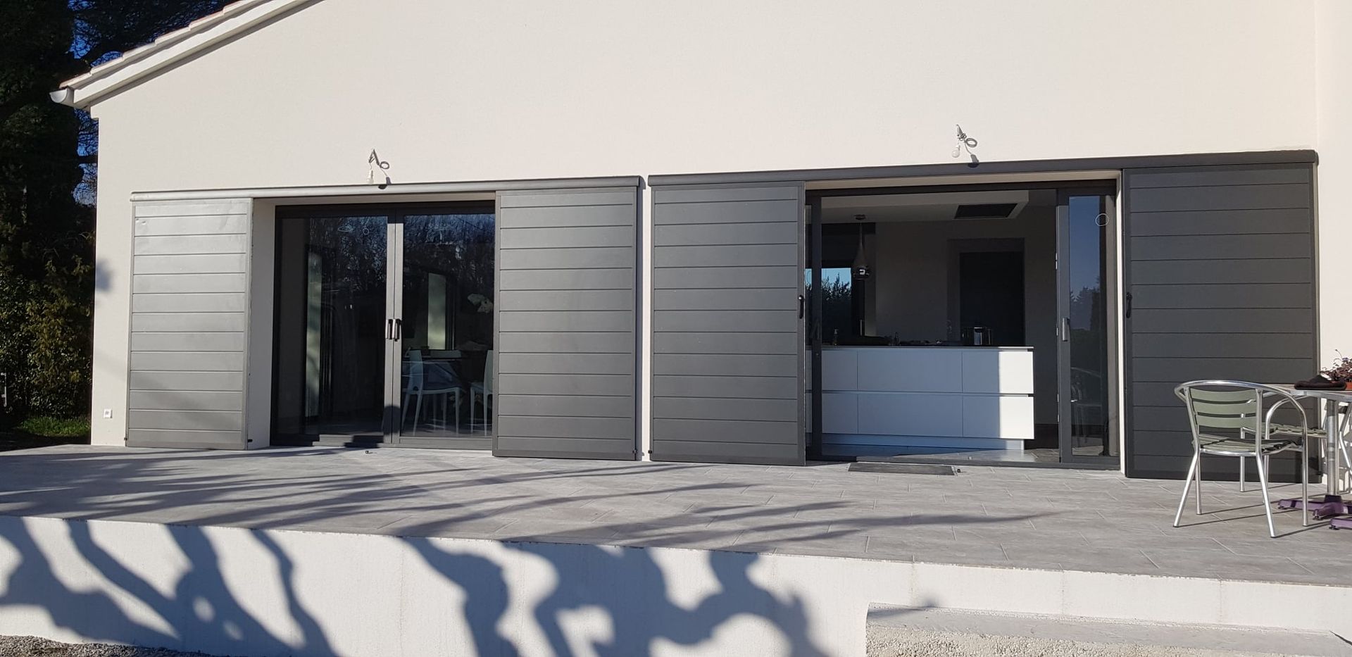 Façade blanche du bâtiment avec deux grandes baies vitrées protégées par des volets coulissants.