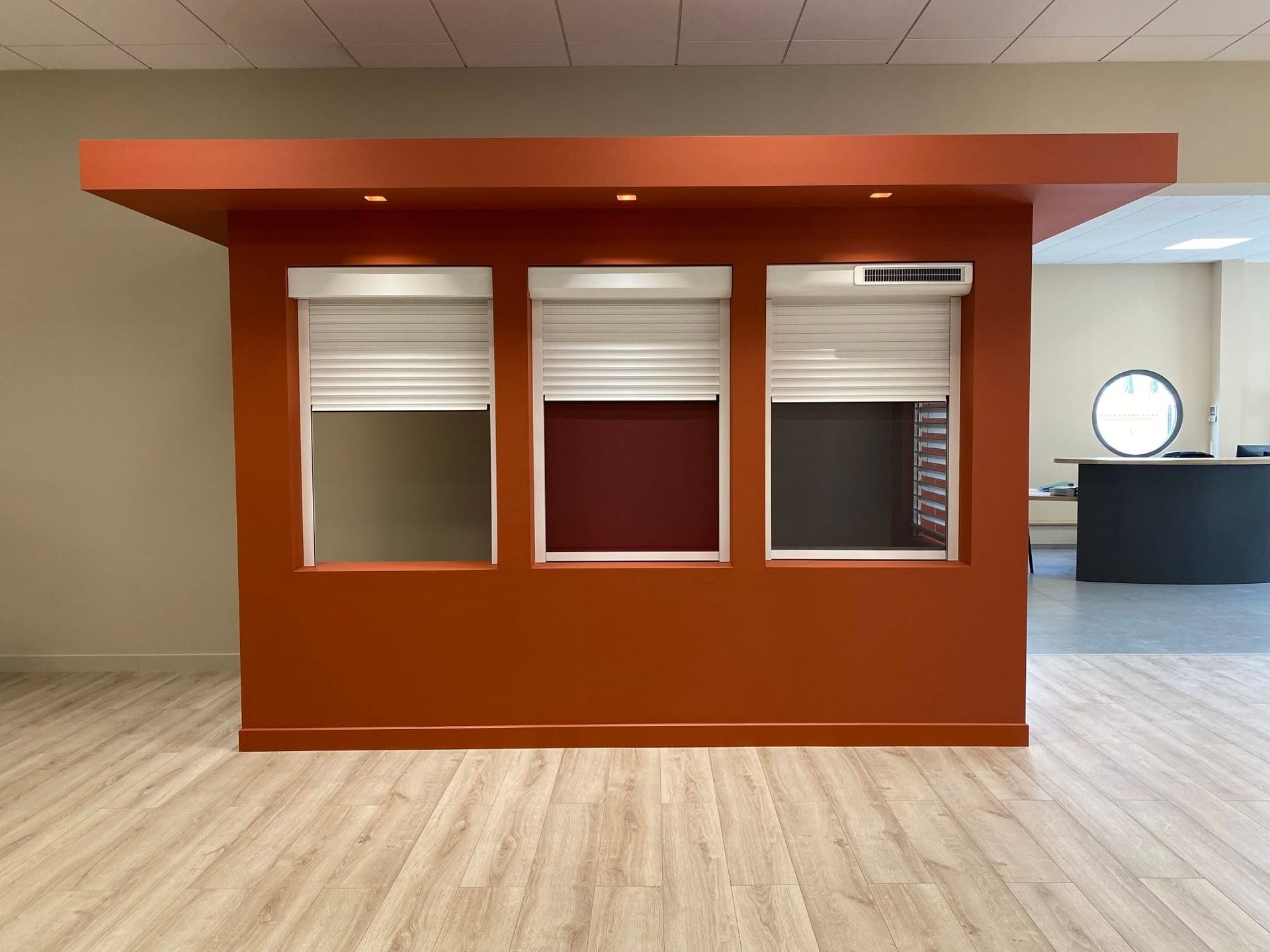 Kiosque de showroom rouge orangé avec trois ouvertures vitrées et des stores baissés.