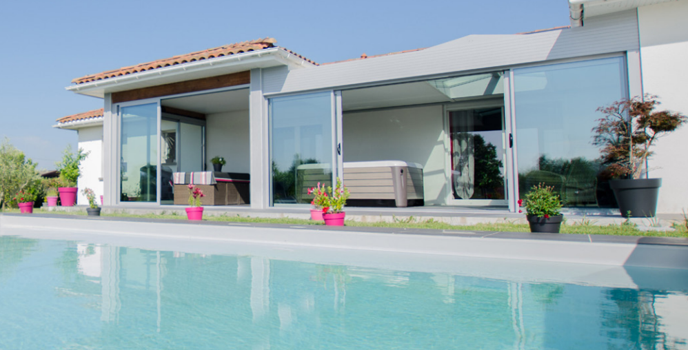 Villa blanche moderne avec vastes baies vitrées donnant sur une piscine turquoise sous un ciel dégagé.