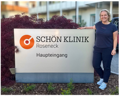 Julia Reher steht neben dem Schild der Schön Klinik Roseneck vor dem Klinikgebäude.