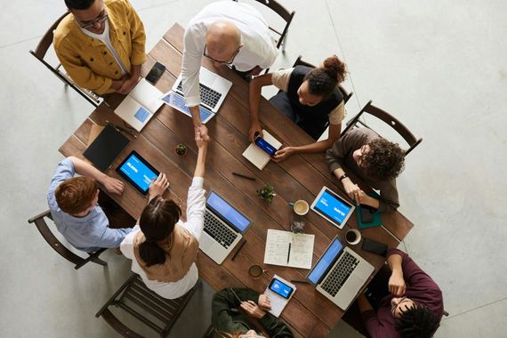 Ein gemischtes Team an einem Holztisch, zwei Personen schütteln sich die Hände nach einem erfolgreichen Team Coaching. 