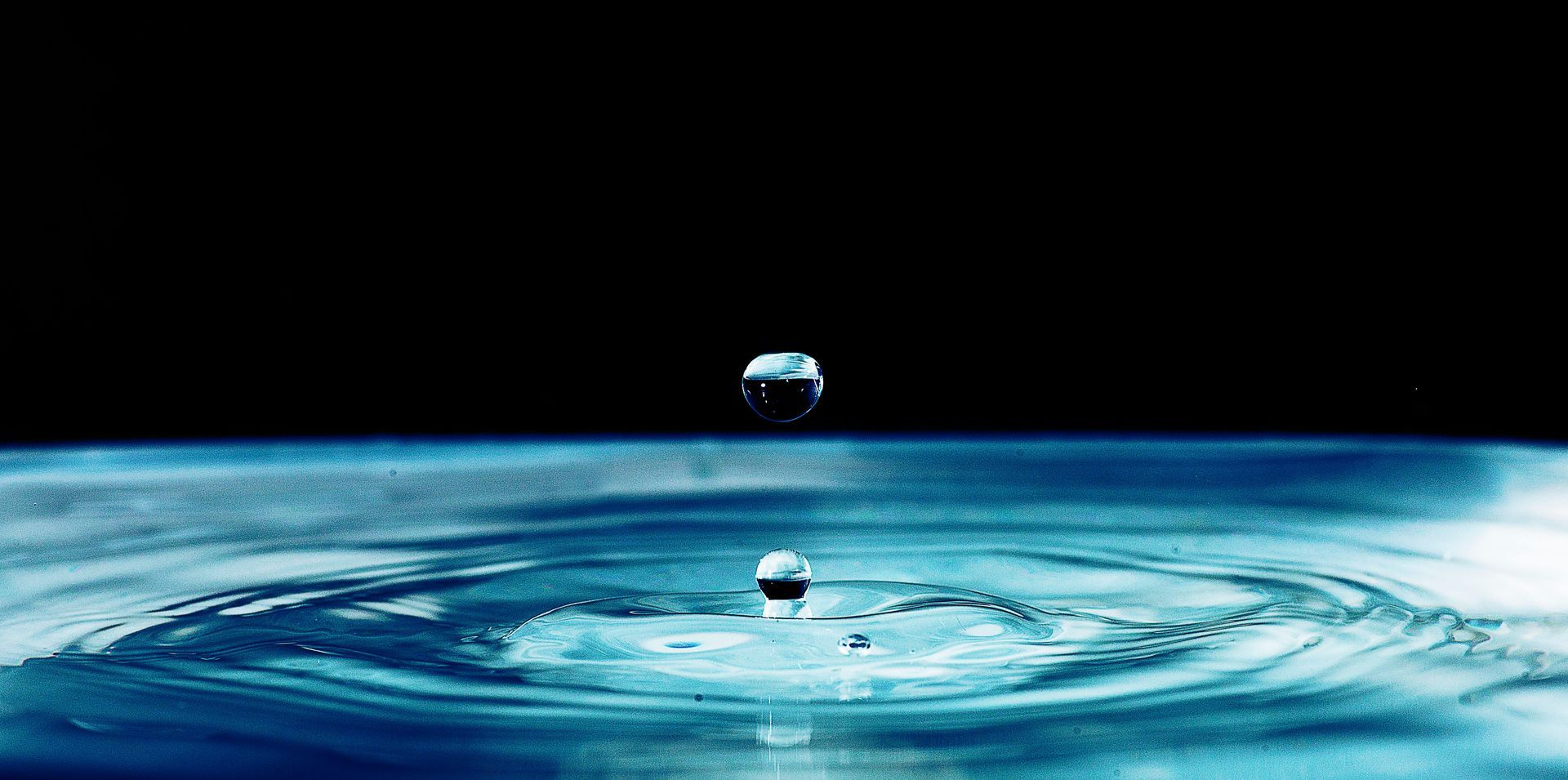 Ein Wassertropfen fällt in eine Wasserpfütze.