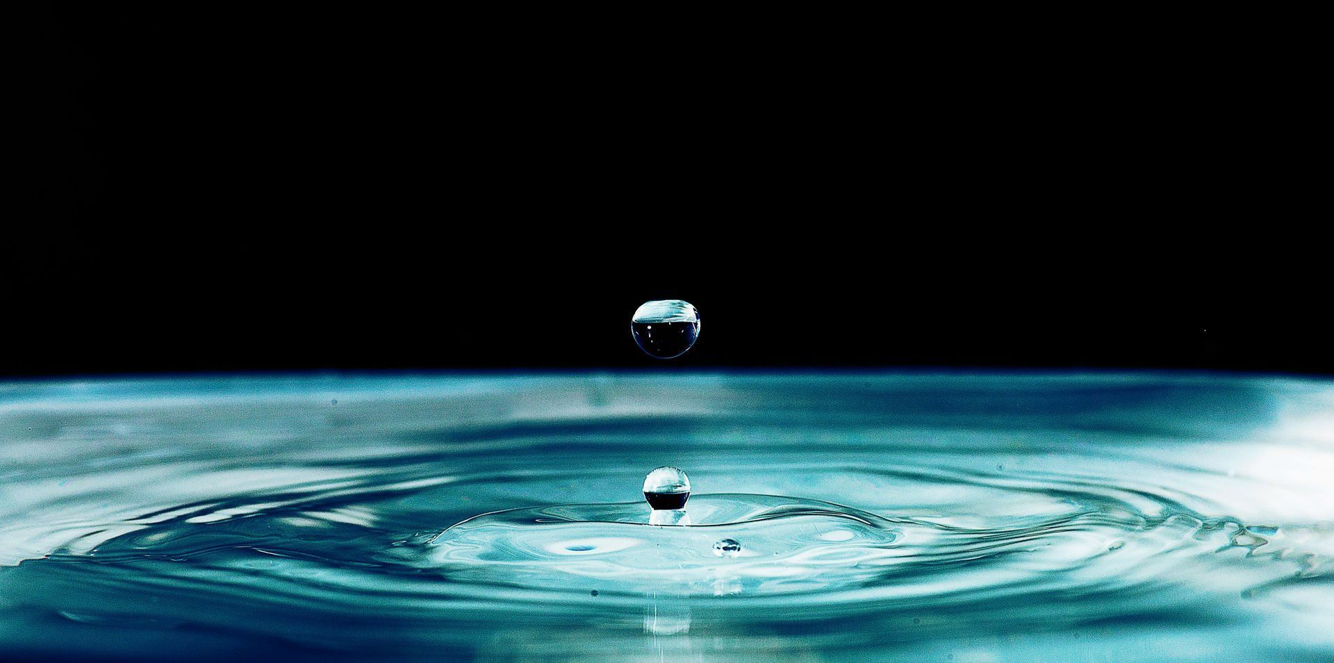Ein Wassertropfen fällt in eine Wasserpfütze.